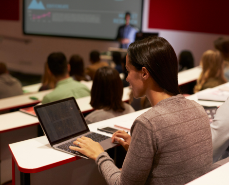 Student taking notes on a laptop in a lecture setting